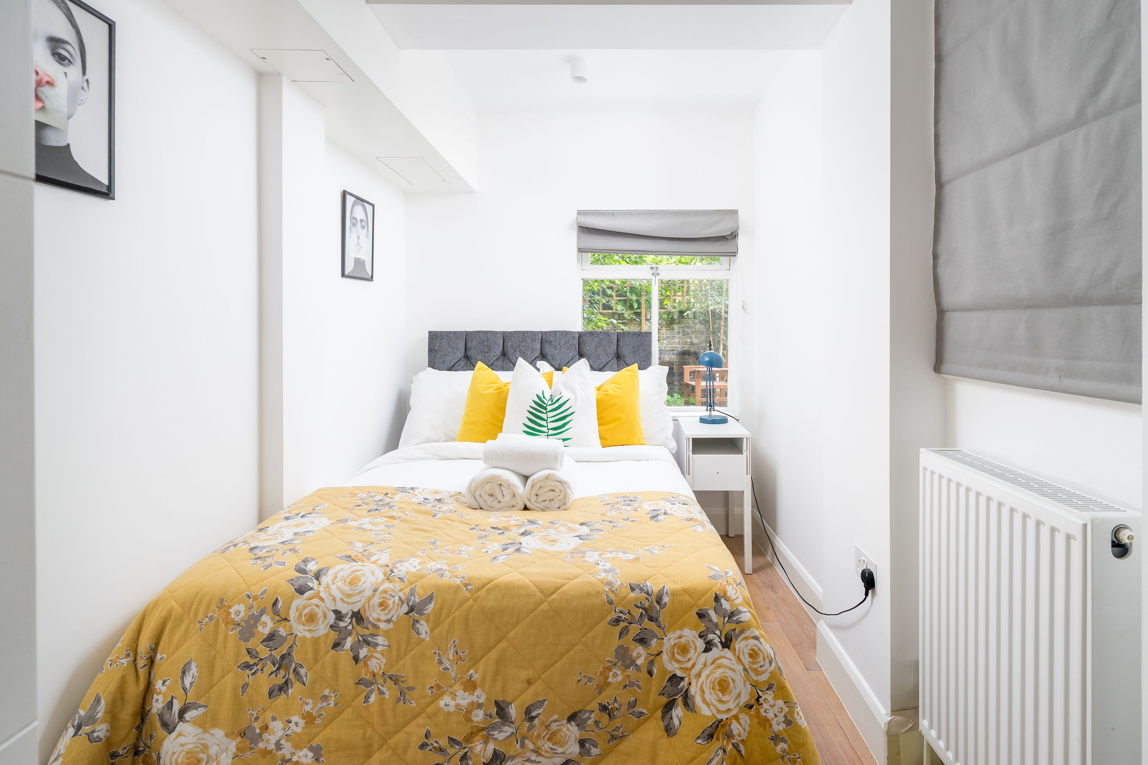 Ein Schlafzimmer mit Bett, Nachttisch, Fenster und Heizkörper.