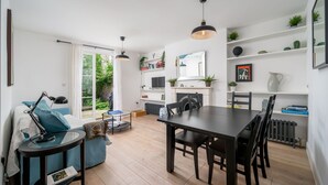 A modern living room with a dining area, white walls, and a large window. - JOIVY Stylish 2-Bed Flat W/ Private Garden In Notting Hill, (London)