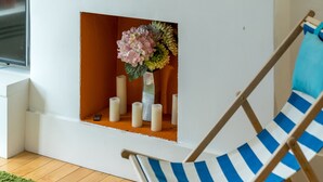 A room with a white wall, a wooden floor, a blue and white striped chair, a small window, and a shelf with candles and flowers. - JOIVY Captivating 2-Bed Flat In Shepherd'S Bush (London)