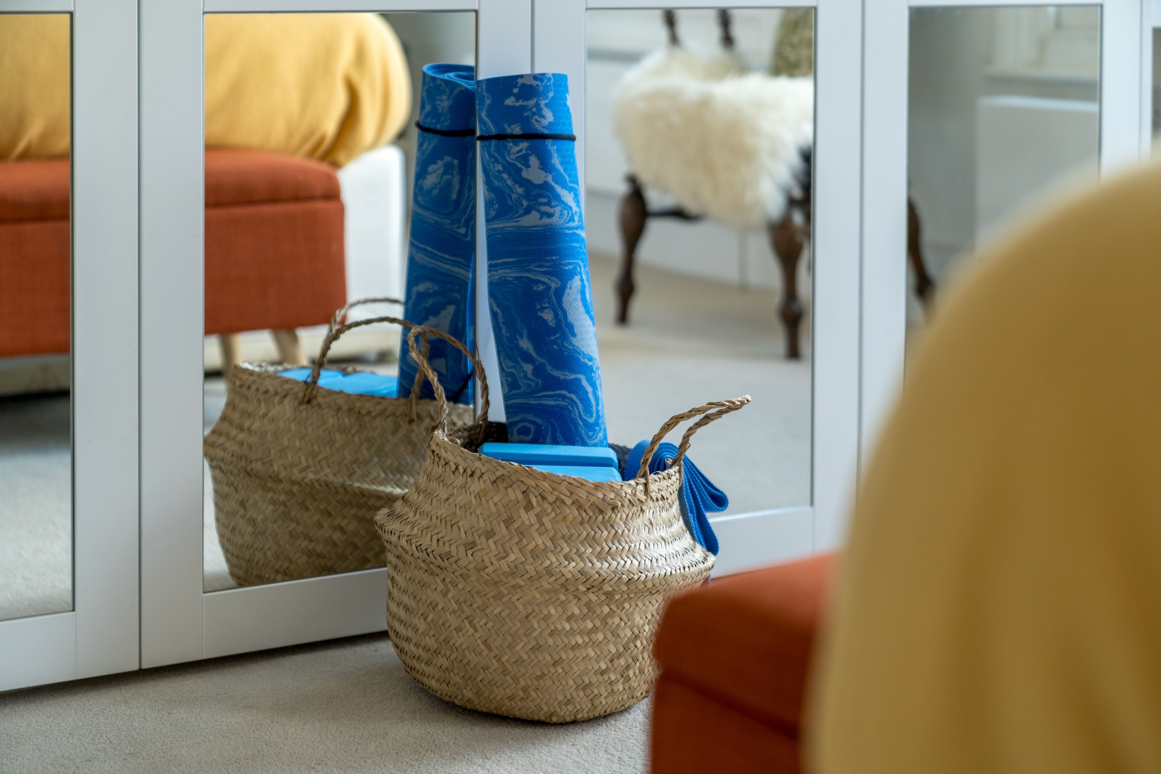 A room with a mirrored wardrobe, a woven basket, and a yoga mat.