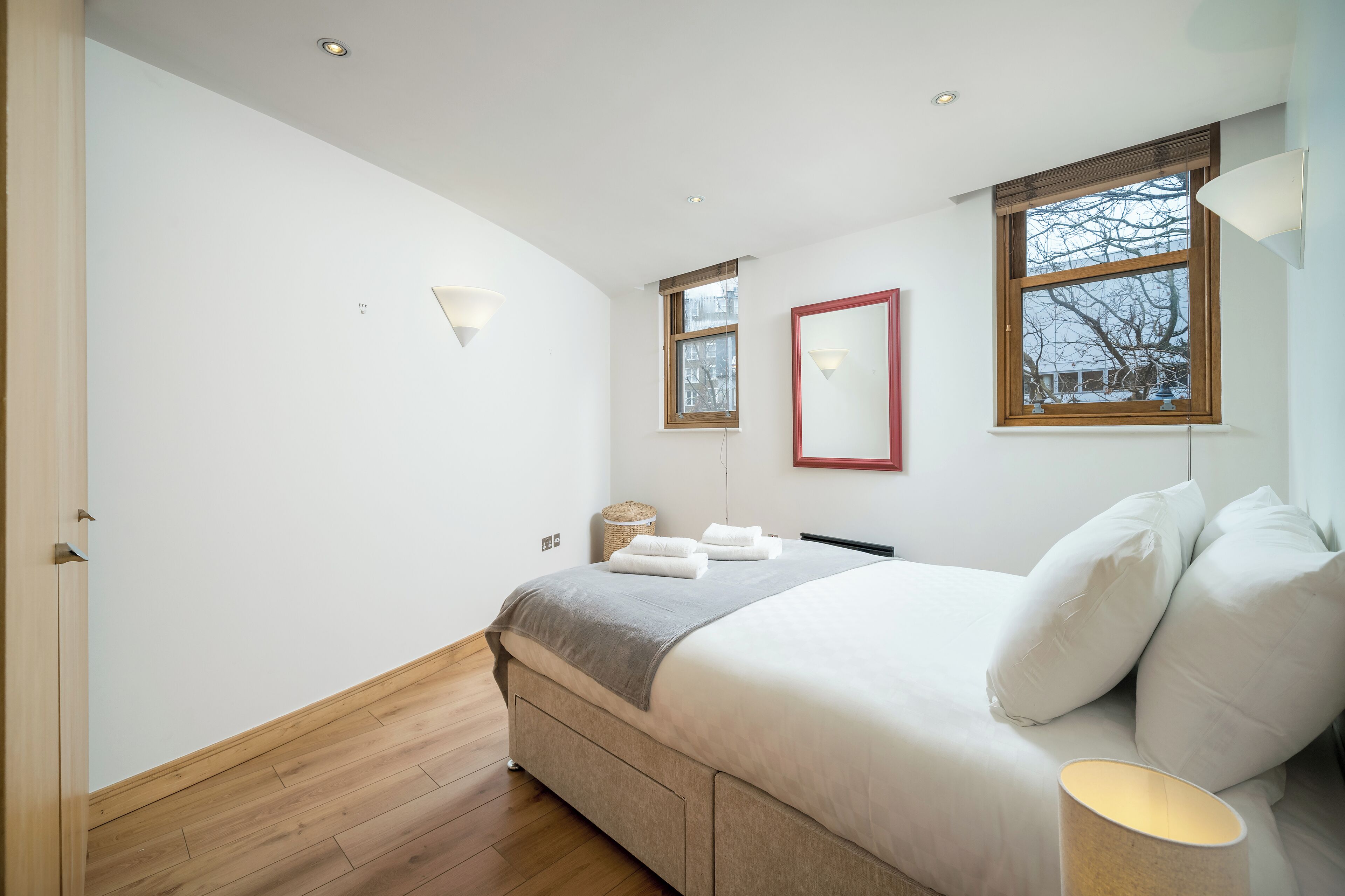 A modern bedroom with a large bed, a bedside table, a lamp, and a window with a view.