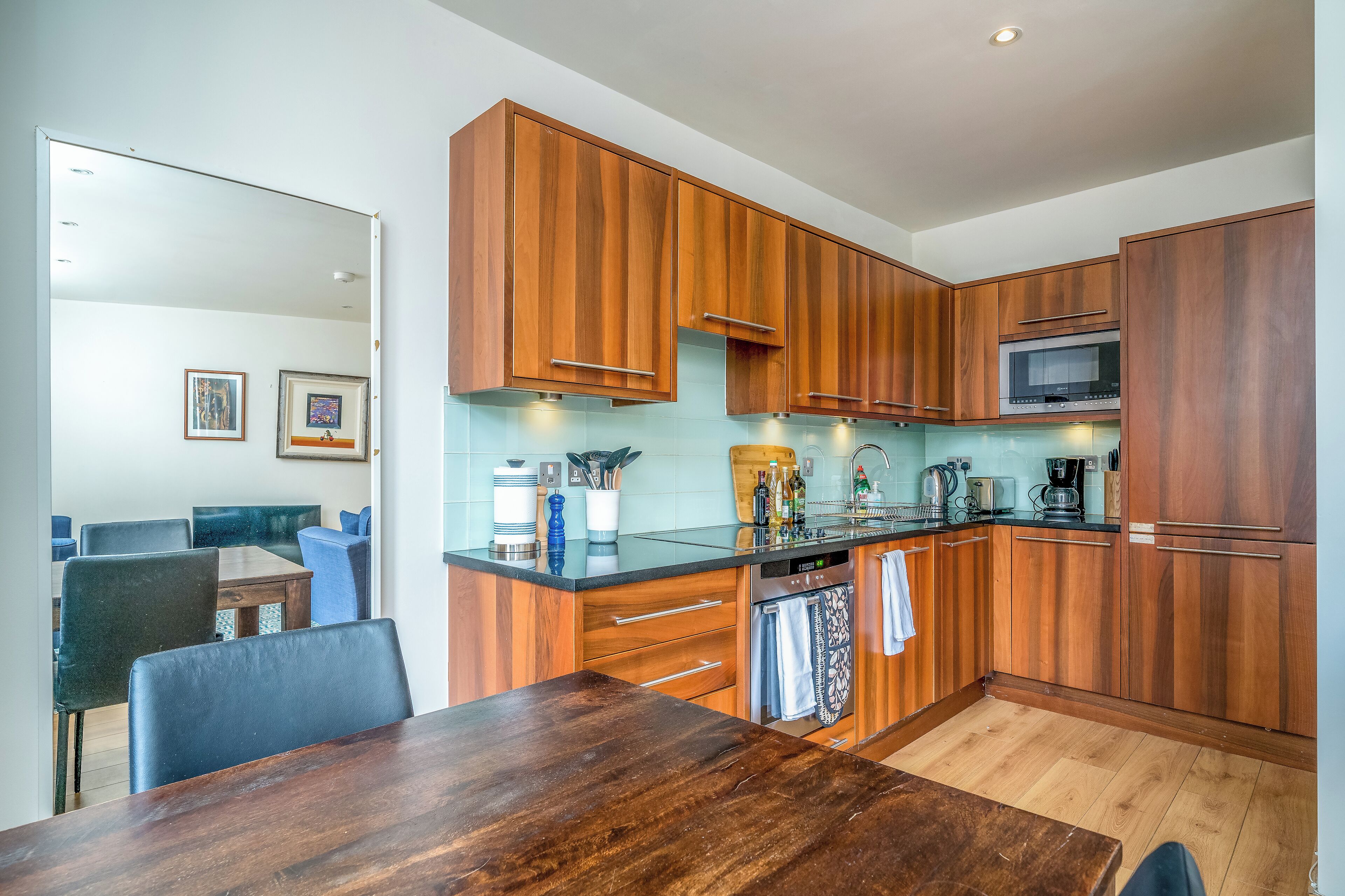 A modern kitchen with wooden cabinets, a built-in microwave, and a dining area with a table and chairs.