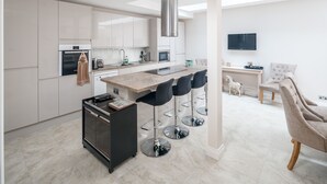 Eine moderne Küche mit Kochinsel, Barhocker, integriertem Backofen und Wand-Fernseher.
