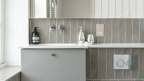 Un baño moderno con un salpicadero de azulejos grises, una encimera blanca, un grifo plateado y una botella de champú.