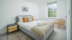 Un dormitorio moderno con una cama, mesitas de noche, una ventana y una silla.