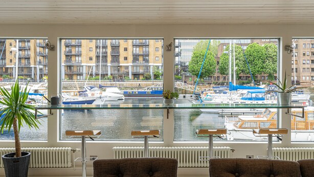 Uitzicht vanuit een raam, met een tafel en stoelen, op een jachthaven met boten en gebouwen.