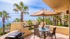 A patio with a grill, table, chairs, and an umbrella. - Peaceful ocean-view condo in an oceanfront community with private beach access! (Cabo San Lucas)