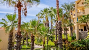 A resort with palm trees, a well-maintained lawn, and a building with balconies. - Peaceful ocean-view condo in an oceanfront community with private beach access! (Cabo San Lucas)