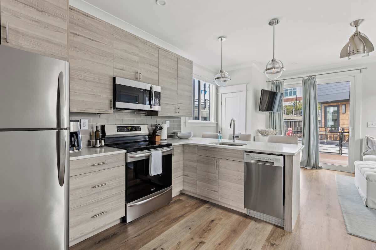 A modern kitchen with stainless steel appliances, wooden cabinetry, and a large window.
