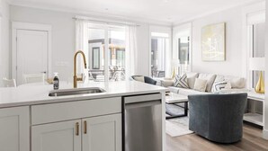 A modern kitchen with a central island, a dining area with a sofa and coffee table, and a view of the outdoors.