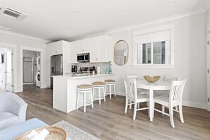 Een moderne keuken met witte kastjes, een centraal eiland en een eethoek met witte stoelen en een ronde tafel.