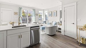 A modern kitchen with a dishwasher, a dining area with a white table and chairs, and a living room with a sofa and a coffee table.