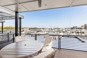 Een balkon met een ronde tafel en stoelen, met uitzicht op een jachthaven met boten.