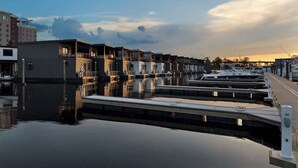A marina with docked boats, a calm water surface, and a row of buildings with balconies.