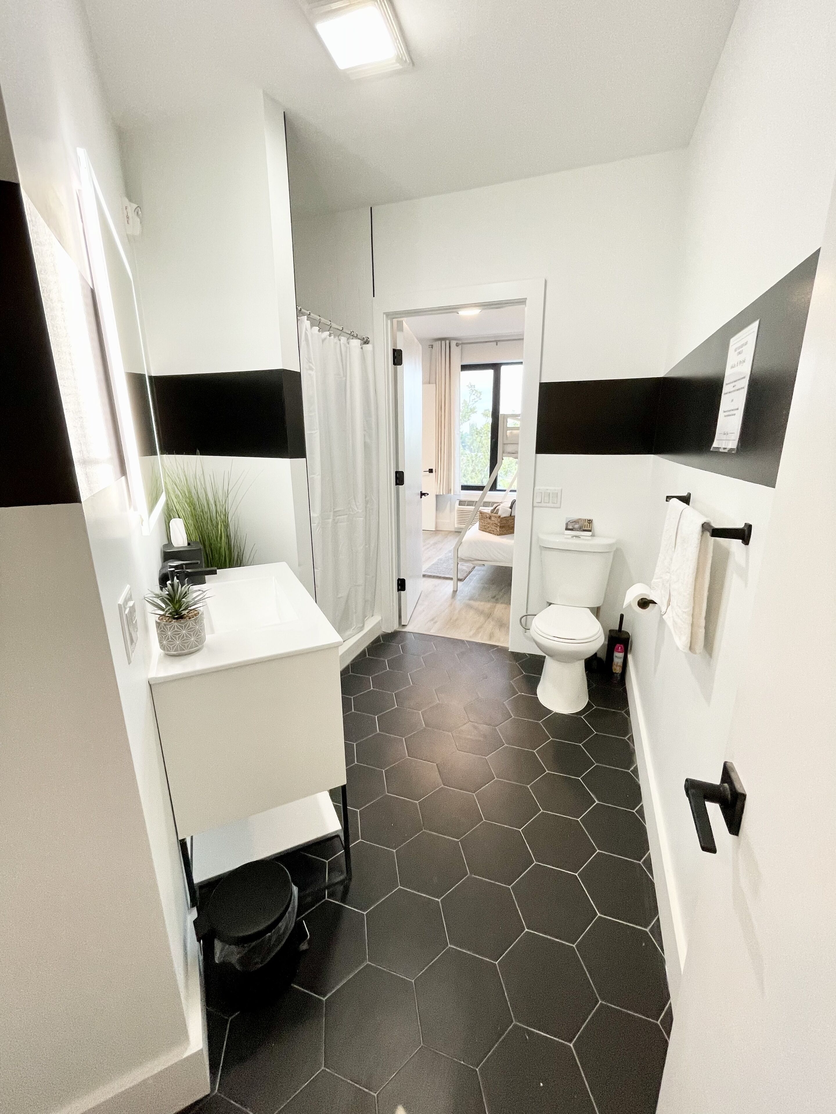 Un baño moderno con un lavamanos blanco, suelo de baldosas blanco y negro, y un inodoro a la vista.