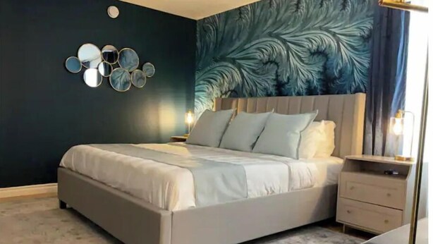 Quarto com cama, mesas de cabeceira, um espelho e uma parede com padrão de folhas.
