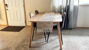 Een eetruimte met een houten tafel, stoelen, een geweven tafelkleed en een deur met deurmat.