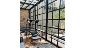 Ein sonnendurchflutetes Zimmer mit einer Glaswand, einem runden Tisch und zwei Stühlen.