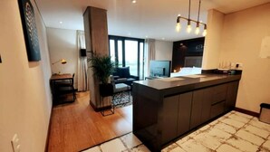 Eine moderne Küche mit einer zentralen Kochinsel, ein Essbereich mit Tisch und Stühlen sowie ein Wohnzimmer mit Sofa und Fernseher.