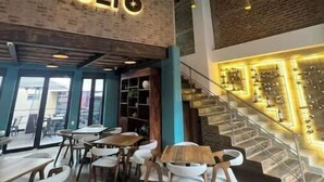 Ein Restaurantinneres mit freiliegenden Backsteinwänden, hängenden Pendelleuchten und einer Treppe mit Glastrennwand. Tische und Stühle sind zum Essen angerichtet.