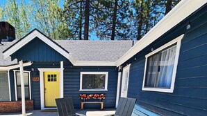 A blue cabin with a yellow door, two Adirondack chairs, and a skateboard on a bench. - Badger Den - Walk to Village, Walk to Shops, Modern, Fenced Yard (Big Bear Lake)