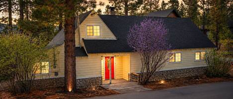 A two-story house with a red door, stone foundation, and a driveway leading to the entrance.