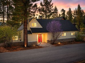 A two-story house with a red door, stone foundation, and a driveway leading to the entrance. - Jaybird Lodge - Walk to Lake & Village, Fireplace, AC (Big Bear Lake)