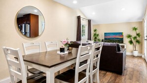 A dining area with a round mirror, a table with chairs, a sofa, a potted plant, and a painting on the wall. - Jaybird Lodge - Walk to Lake & Village, Fireplace, AC (Big Bear Lake)