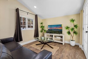 A living room with a glass coffee table, leather sofa, and a painting on the wall.