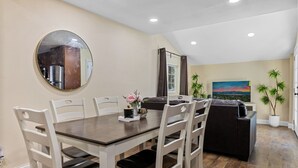 A dining area with a round mirror, a dark wooden table, white chairs, and a black sofa.