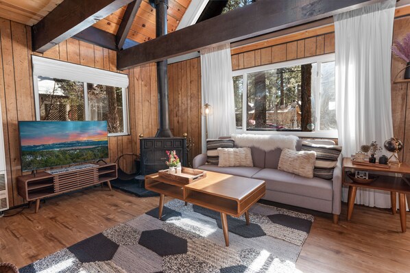 A cozy living room with wooden walls, a large window, a fireplace, and a comfortable sofa.