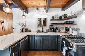 A modern kitchen with dark blue cabinets, a stainless steel stove, and a white marble countertop.