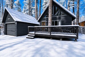 A cabin with a garage, a deck, and a staircase leading to the entrance. - Bearadise - Modern, Fireplace, Fenced Yard, Deck (Big Bear City)