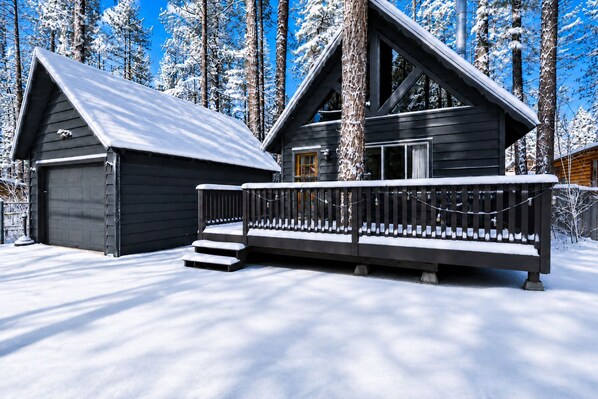 A cabin with a garage, a deck, and a staircase leading to the entrance. - Bearadise - Modern, Fireplace, Fenced Yard, Deck (Big Bear City)