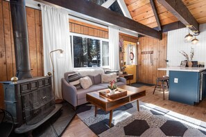 Un salon chaleureux avec une cheminée, un canapé, une table basse et un coin cuisine avec un bar.