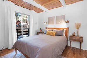 A bedroom with a large bed, wooden headboard, two bedside tables with lamps, and a view of a wooden deck outside.