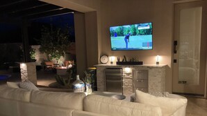 Una sala de estar moderna con un sofá blanco, un televisor de pantalla plana en la pared, un pilar de piedra y un refrigerador pequeño.