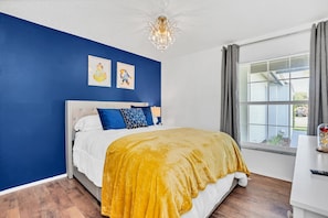 Un dormitorio con cama, candelabro, ventana con cortinas y obras de arte en la pared.