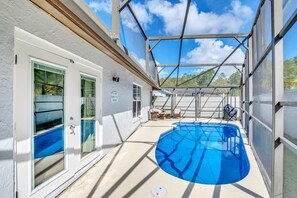 A covered outdoor swimming pool area with a glass door entrance, a covered seating area, and a view of the surrounding landscape.