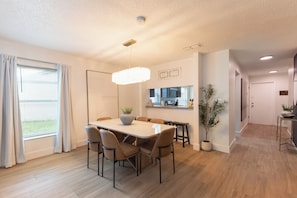 A modern dining area with a table and chairs, a ceiling light, and a view of the kitchen.