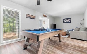 Una sala de estar moderna con mesa de billar, un sofá y un amplio ventanal con persianas.