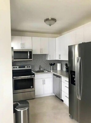 Enjoy cooking in this well-equipped kitchen with stainless steel appliances, white cabinetry, and a tiled backsplash.