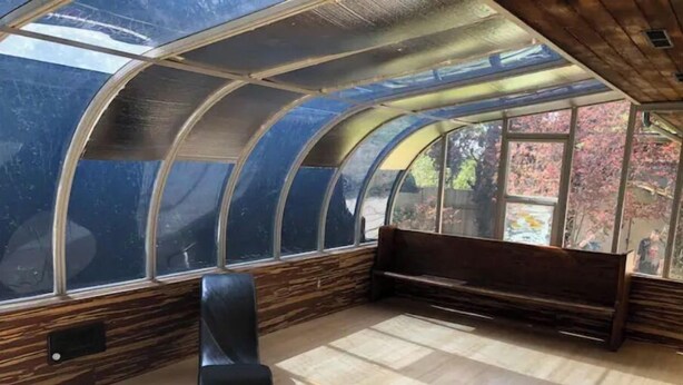 A room with a curved ceiling, wooden walls, a bench, and a window with a view of trees. - 3-Bedroom house with Sunroom (Seattle)