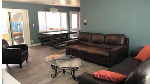 A living room with a brown leather sofa, a glass coffee table, and a pool table. - 3-Bedroom house with Sunroom (Seattle)