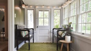 Ein Zimmer mit einem grünen Teppich, zwei schwarzen Bänken mit gestreiften Kissen, einem kleinen runden Tisch mit einer Pflanze und einer weißen Tür mit einem Fenster darüber.