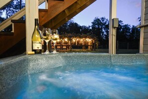 A hot tub area with a wooden structure overhead, a bottle, and glasses.