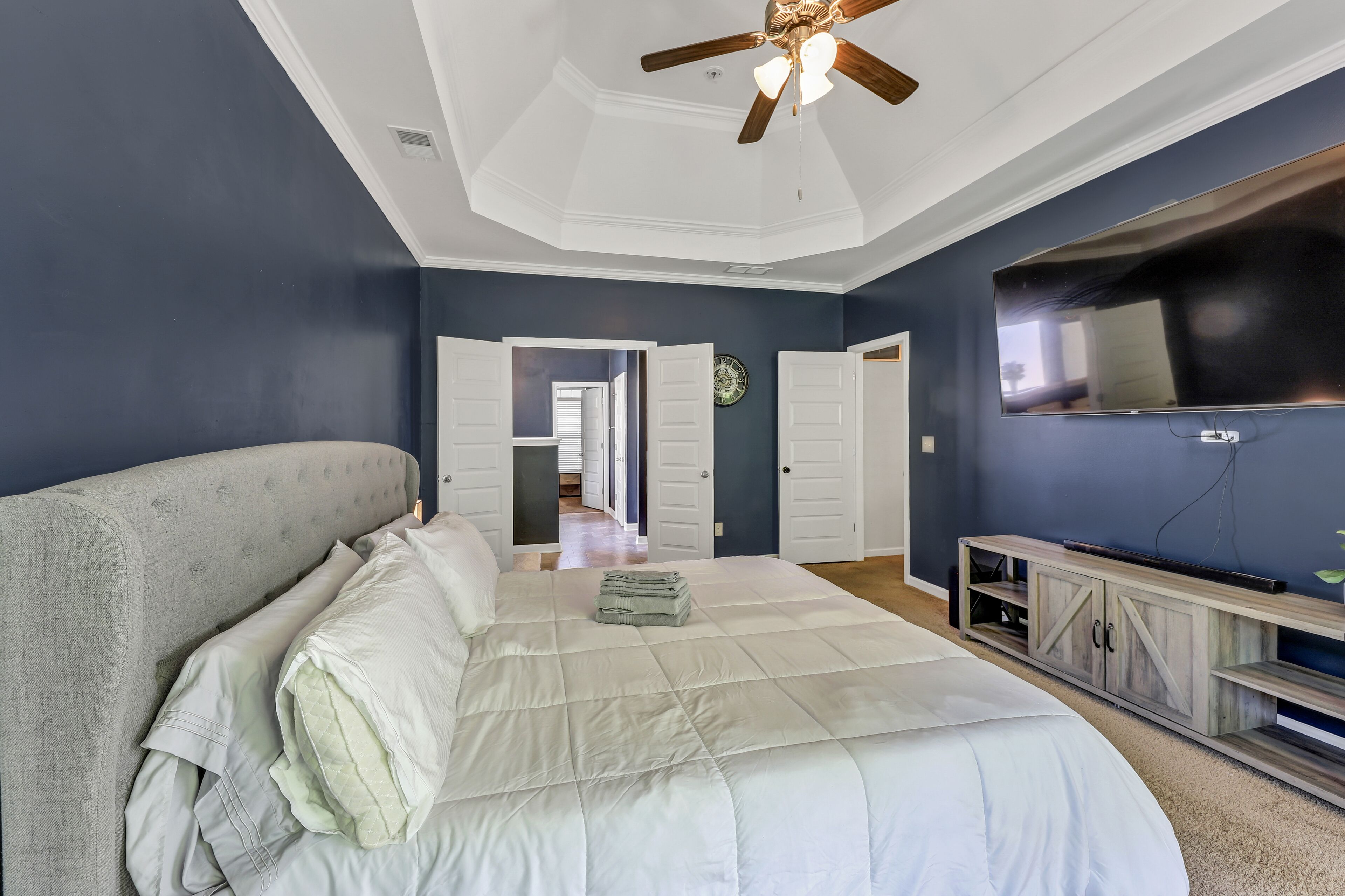 Camera da letto con un letto grande, un ventilatore a soffitto, una TV e una porta che dà su un'altra stanza.