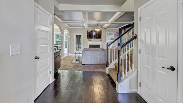 A hallway with a dark wooden floor, white walls, and a staircase with a white railing.