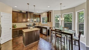 A modern kitchen with wooden cabinets, a central island, and a dining area with a table and chairs.