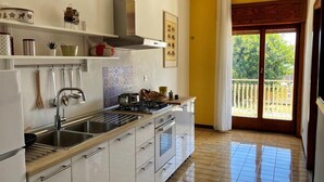 A kitchen with white cabinets, a stove, and a sink. There is a window with a view of greenery outside. - Vacation home IL NIDO (Aeolian Islands boarding) WiFi/park free. CIR 19083049C21 (Milazzo)